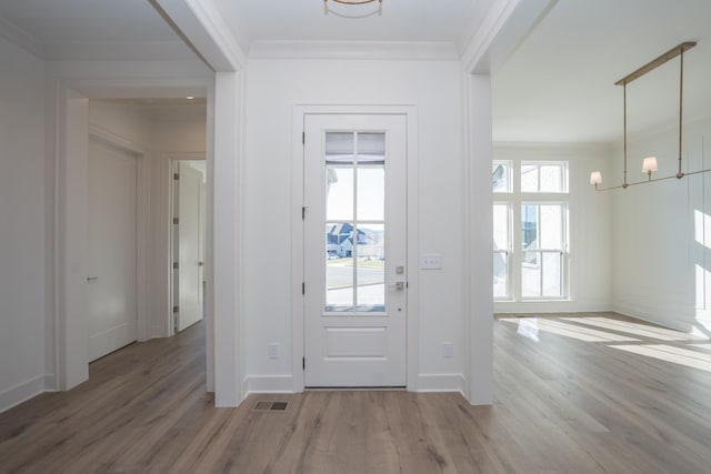 foyer entrance with a healthy amount of sunlight, visible vents, wood finished floors, and ornamental molding