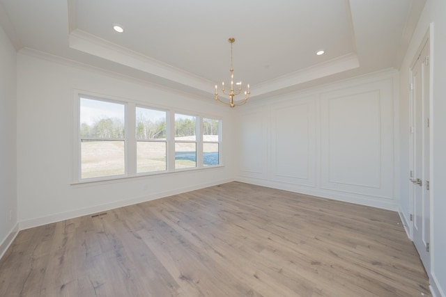 spare room with a tray ceiling, crown molding, a notable chandelier, light wood finished floors, and recessed lighting