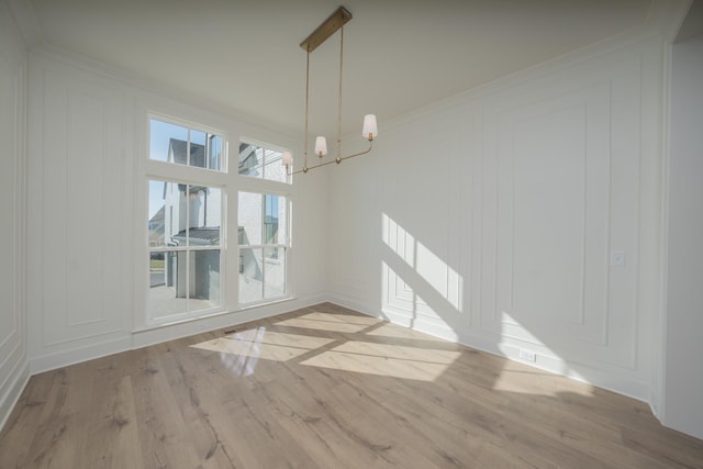 unfurnished dining area with an inviting chandelier, ornamental molding, a decorative wall, and wood finished floors