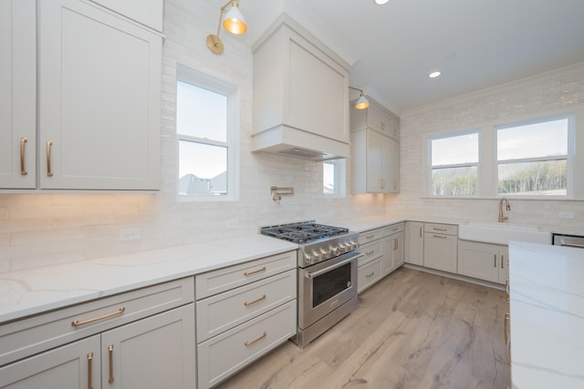 kitchen with stainless steel range, decorative backsplash, custom range hood, light stone countertops, and a sink