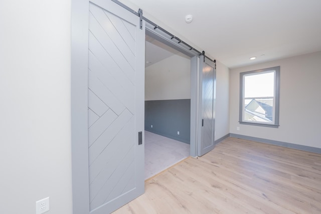 empty room featuring light wood finished floors, a barn door, and baseboards