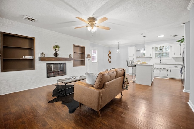 living area featuring built in features, visible vents, dark wood-style flooring, and a textured ceiling