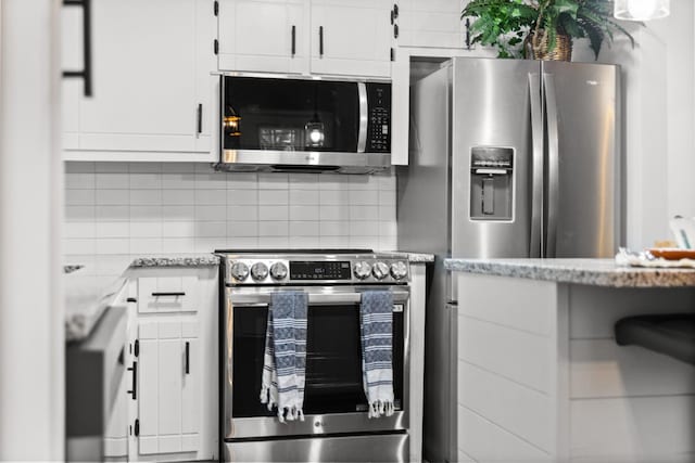 kitchen featuring appliances with stainless steel finishes, white cabinetry, backsplash, and light stone countertops