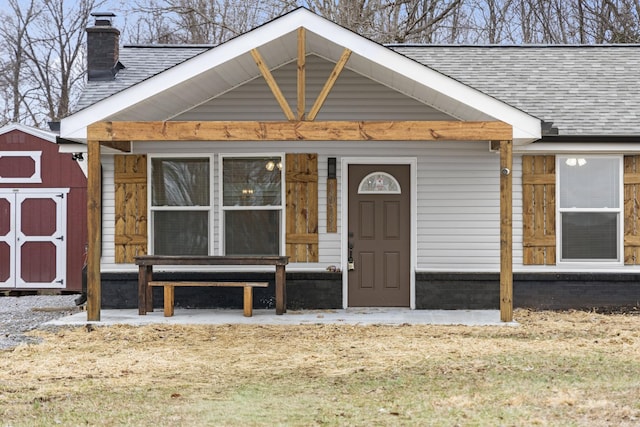 entrance to property featuring a shingled roof and a chimney