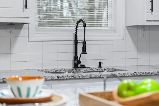 room details featuring white cabinets, a sink, backsplash, and light stone countertops