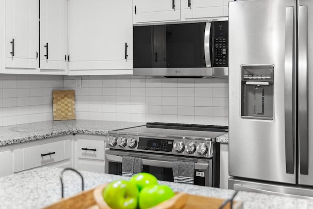 kitchen featuring white cabinets, light stone countertops, appliances with stainless steel finishes, and decorative backsplash