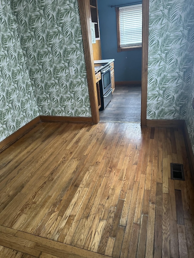 kitchen with dark wood-type flooring, visible vents, baseboards, electric stove, and wallpapered walls