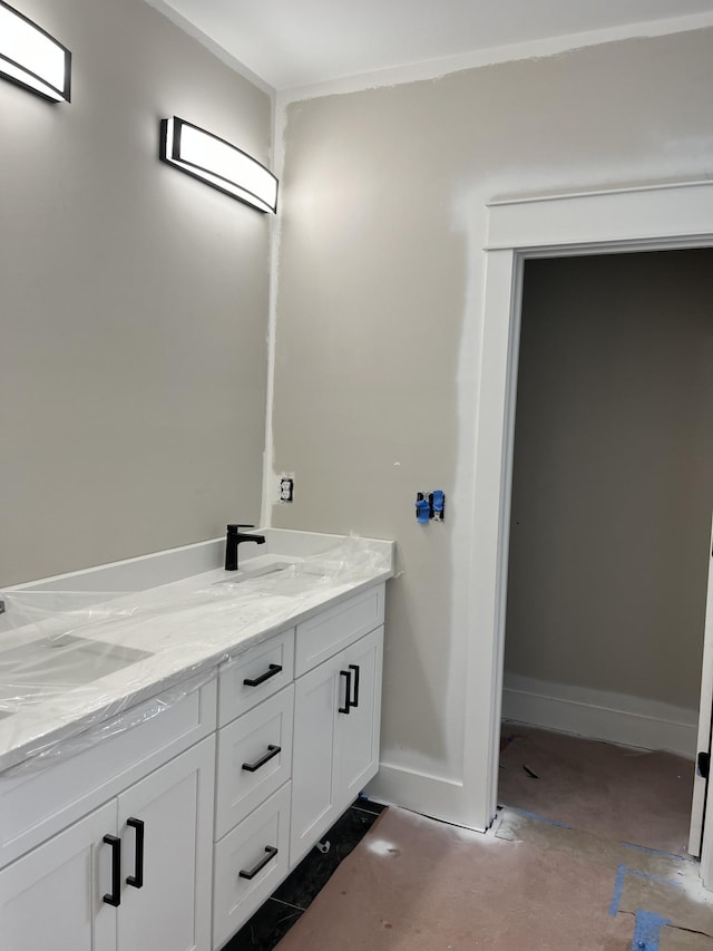 bathroom featuring concrete flooring, double vanity, a sink, and baseboards