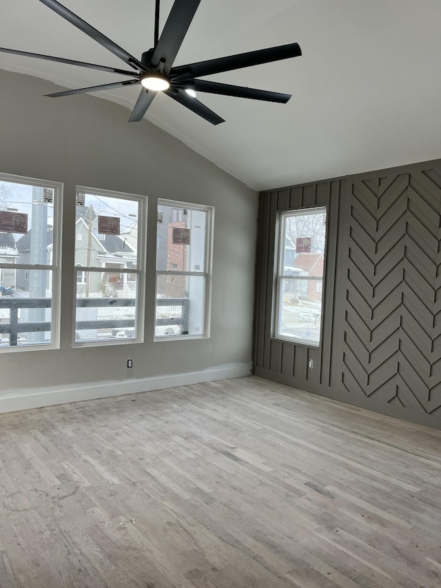 empty room with lofted ceiling, ceiling fan, light wood-style flooring, and baseboards