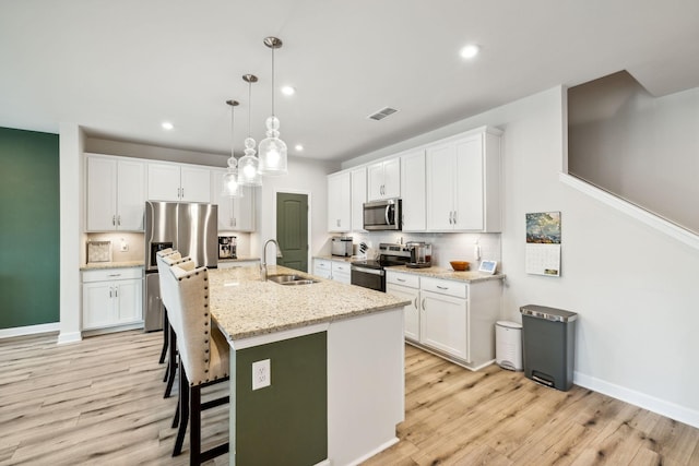 kitchen featuring light wood-style flooring, stainless steel appliances, a sink, visible vents, and white cabinets