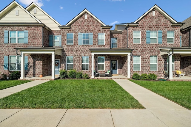 multi unit property featuring covered porch, brick siding, and a front lawn