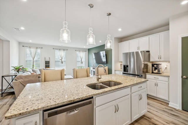 kitchen with a sink, light wood-style floors, open floor plan, appliances with stainless steel finishes, and a center island with sink