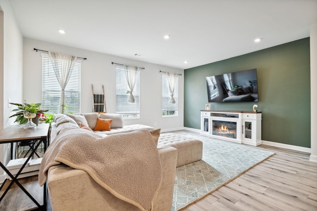 living room featuring a glass covered fireplace, recessed lighting, baseboards, and wood finished floors