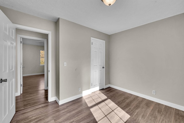 unfurnished bedroom with dark wood-style floors, a textured ceiling, and baseboards