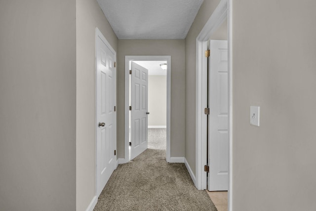 corridor with a textured ceiling, baseboards, and light colored carpet