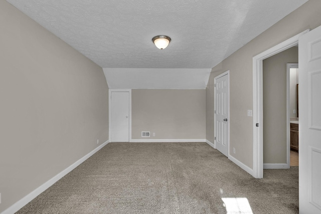 carpeted empty room with vaulted ceiling, a textured ceiling, visible vents, and baseboards