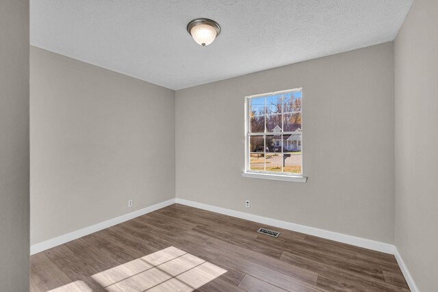 spare room featuring a textured ceiling, wood finished floors, visible vents, and baseboards