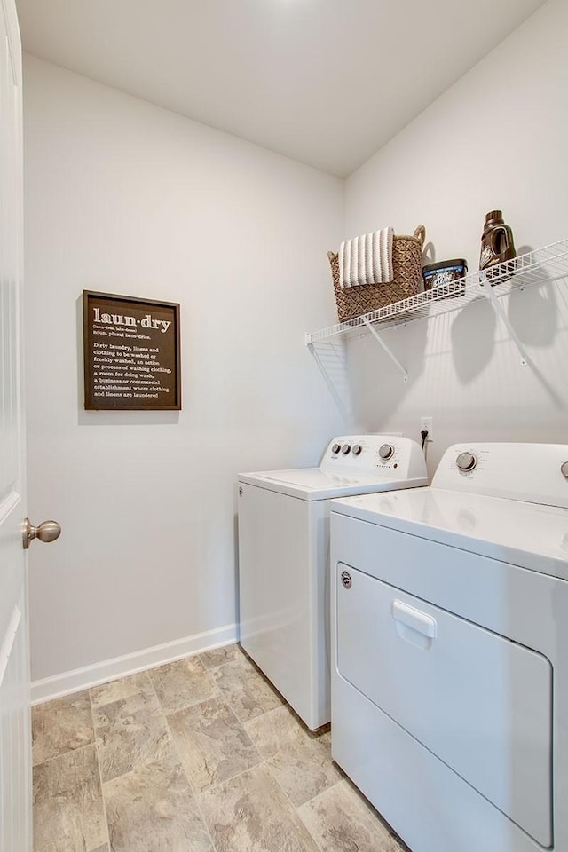 clothes washing area featuring laundry area, stone finish floor, washing machine and dryer, and baseboards