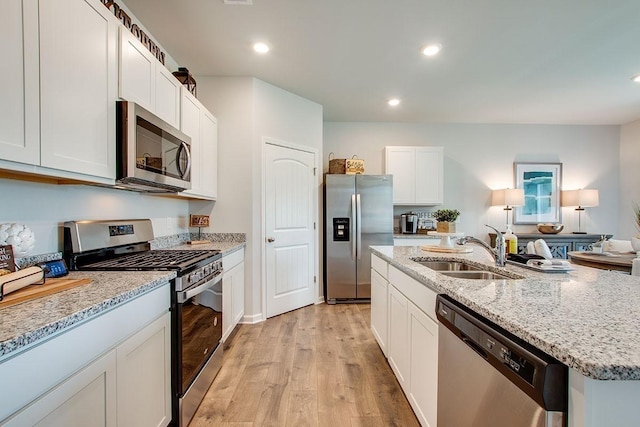 kitchen with light stone counters, light wood finished floors, appliances with stainless steel finishes, a sink, and an island with sink