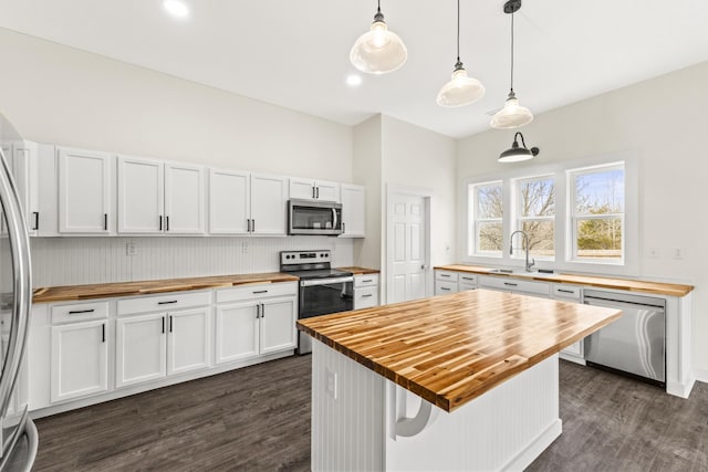 kitchen featuring dark wood-style floors, appliances with stainless steel finishes, white cabinetry, a sink, and butcher block countertops