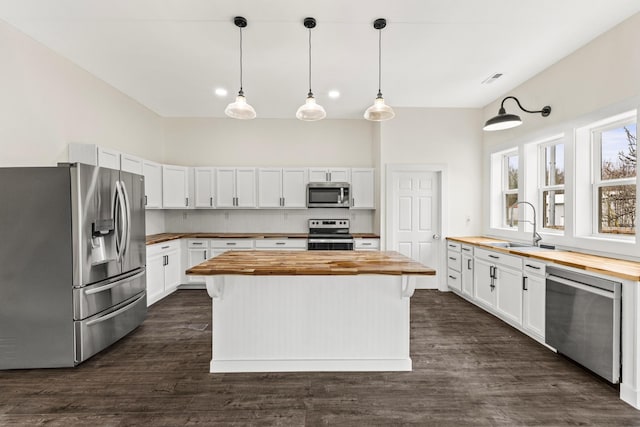 kitchen with butcher block counters, appliances with stainless steel finishes, dark wood-type flooring, and a sink