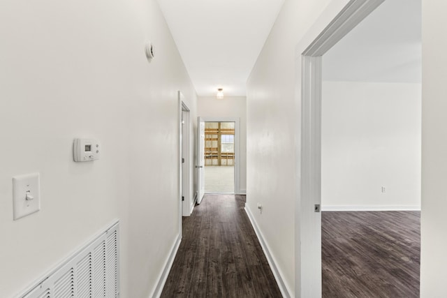 hall featuring dark wood-style flooring, visible vents, and baseboards