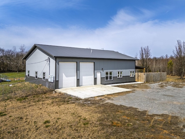 back of property featuring metal roof, a detached garage, fence, and an outdoor structure