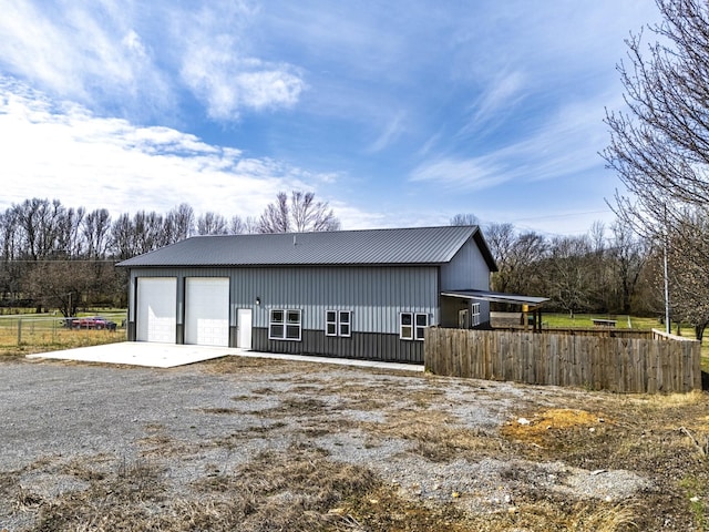 exterior space featuring a garage, fence, metal roof, and an outdoor structure