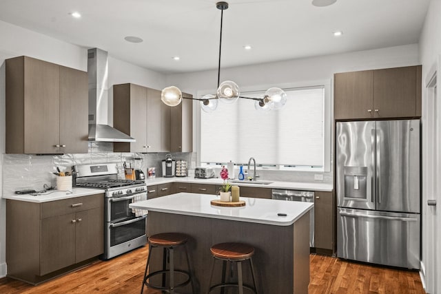 kitchen with wall chimney exhaust hood, appliances with stainless steel finishes, a breakfast bar, wood finished floors, and a sink