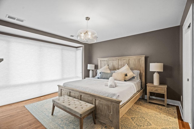 bedroom featuring an inviting chandelier, visible vents, and wood finished floors