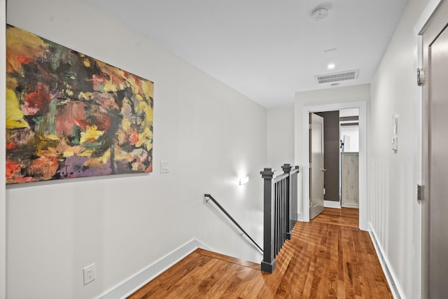 corridor featuring baseboards, visible vents, wood finished floors, and an upstairs landing