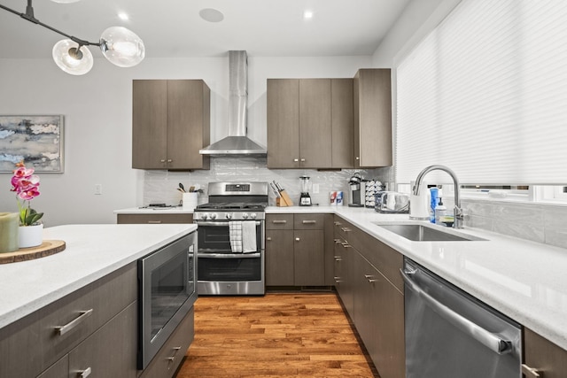 kitchen with wall chimney exhaust hood, appliances with stainless steel finishes, a sink, and light countertops