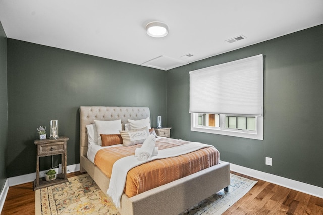 bedroom with attic access, visible vents, baseboards, and wood finished floors