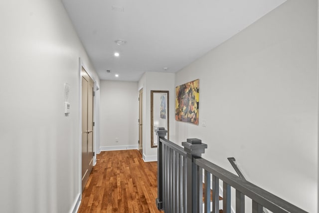 corridor with recessed lighting, wood finished floors, an upstairs landing, and baseboards