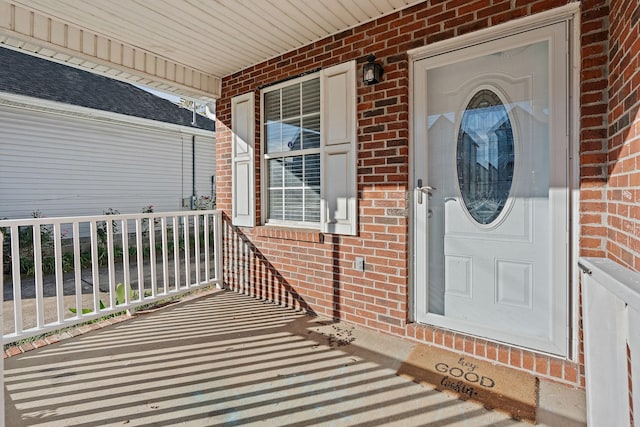 doorway to property featuring a porch and brick siding