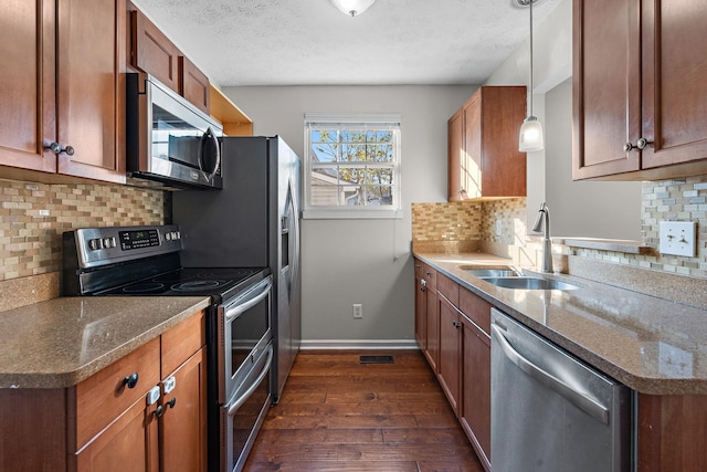 kitchen featuring appliances with stainless steel finishes, brown cabinetry, dark wood-type flooring, a sink, and baseboards