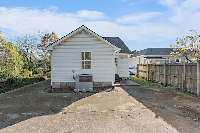 rear view of property with central AC unit, a shingled roof, and fence