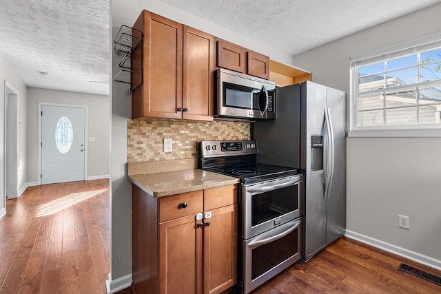 kitchen with tasteful backsplash, visible vents, brown cabinetry, dark wood-style floors, and stainless steel appliances