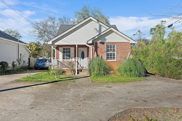 bungalow featuring driveway, a shingled roof, a porch, and brick siding