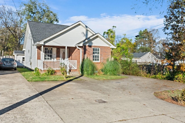 bungalow-style home featuring covered porch, driveway, brick siding, and roof with shingles