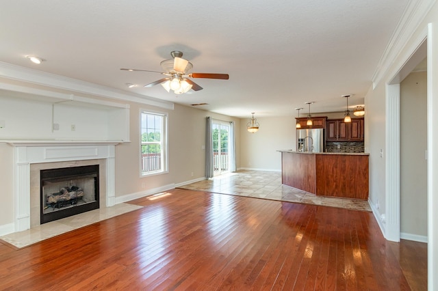 unfurnished living room with ceiling fan, a fireplace, ornamental molding, and hardwood / wood-style floors