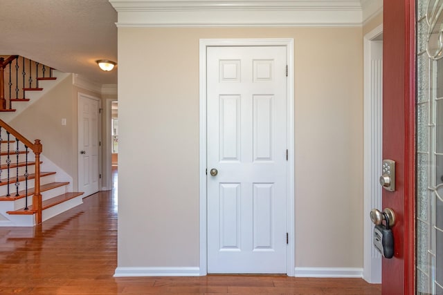 entrance foyer with ornamental molding, stairway, baseboards, and wood finished floors