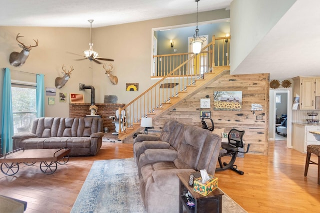 living area with light wood-type flooring, a wood stove, a towering ceiling, and stairs