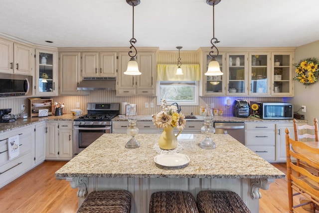 kitchen with appliances with stainless steel finishes, a kitchen island, a breakfast bar, and under cabinet range hood