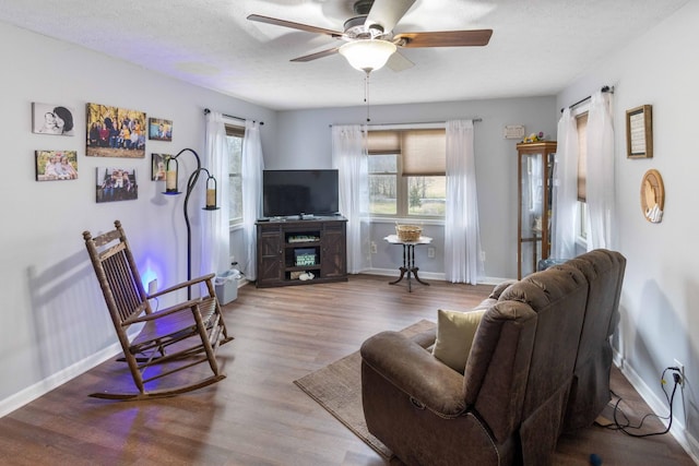 living room with ceiling fan, a textured ceiling, baseboards, and wood finished floors