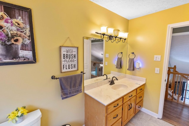 bathroom with toilet, a textured ceiling, vanity, and baseboards