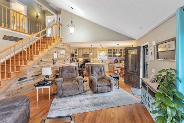 living room featuring high vaulted ceiling, light wood-type flooring, visible vents, and stairway