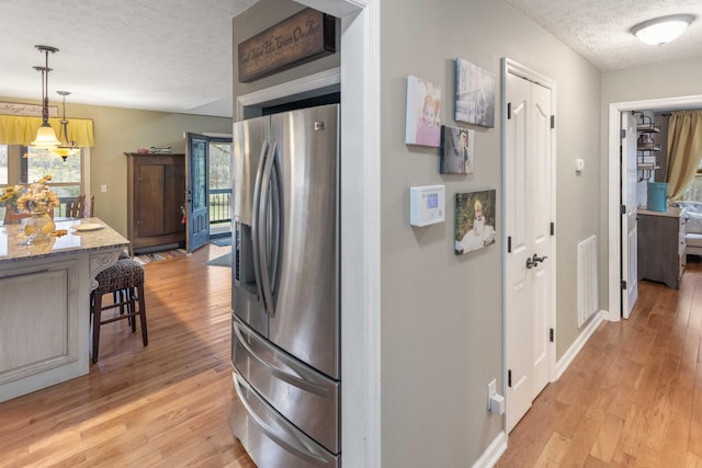 kitchen featuring light stone counters, light wood-style flooring, a textured ceiling, stainless steel fridge, and a kitchen breakfast bar