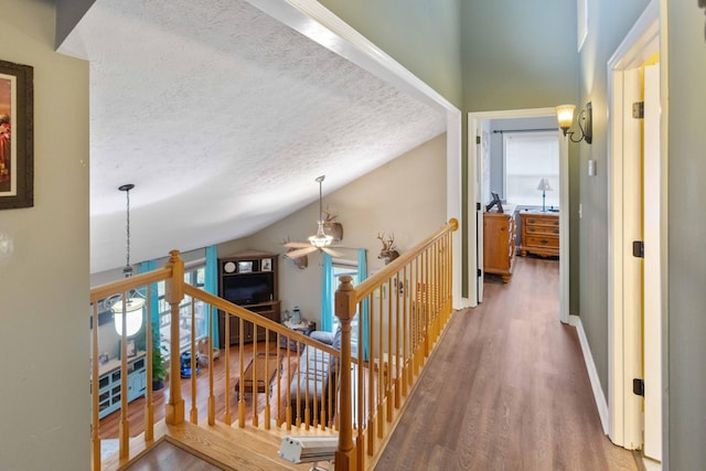 hall featuring a textured ceiling, high vaulted ceiling, wood finished floors, an upstairs landing, and baseboards