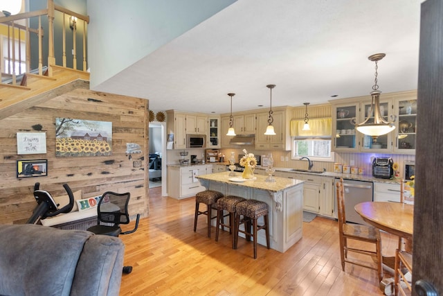 kitchen featuring stainless steel appliances, a kitchen island, a sink, light wood-style floors, and a kitchen bar